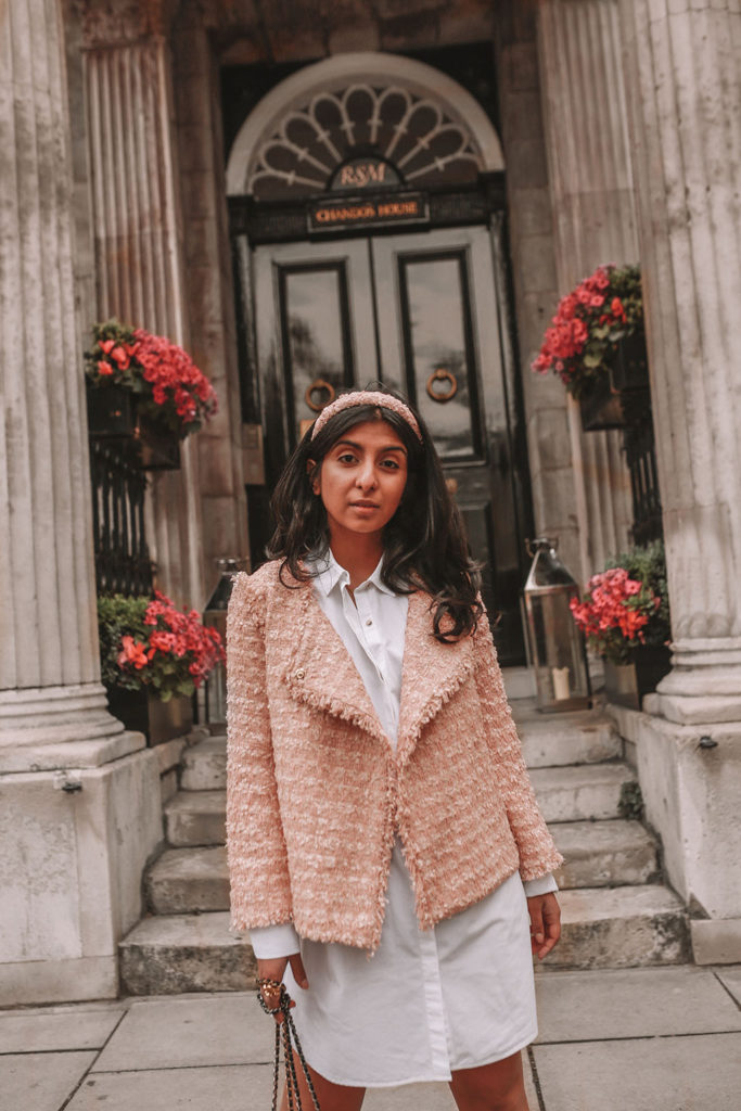 Luxury fashion blogger Shloka Narang of The Silk Sneaker shares how to style a tweed jacket for a luxury Chanel look in a white shirt dress, Chanel backpack, Prada strappy sandals and headband