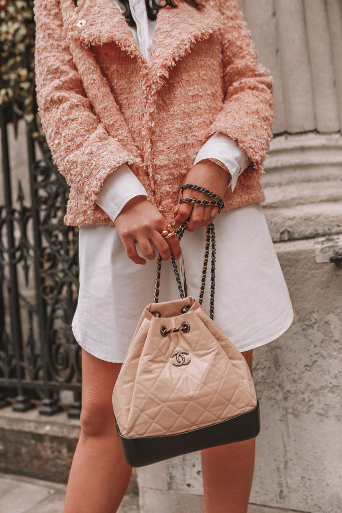 Luxury fashion blogger Shloka Narang of The Silk Sneaker shares how to style a tweed jacket for a luxury Chanel look in a white shirt dress, Chanel backpack, Prada strappy sandals and headband