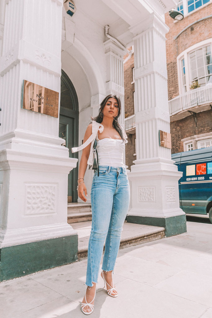 Luxury fashion blogger Shloka Narang of The Silk Sneaker shares a cute summer outfit for the heatwave styling blue jeans with a white summer blouse featuring Paige and Prada