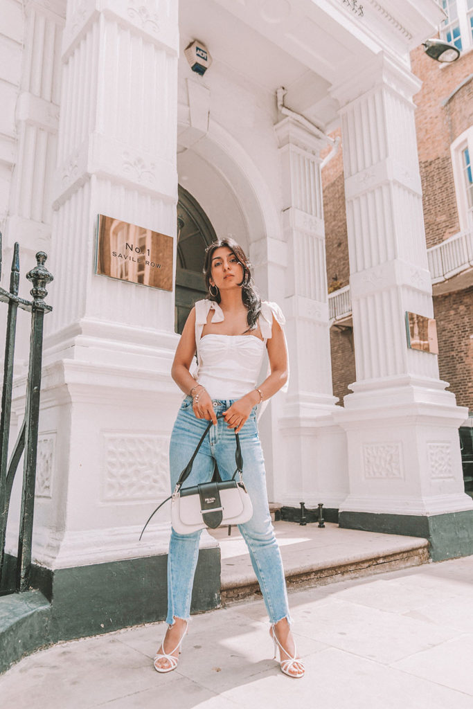 Luxury fashion blogger Shloka Narang of The Silk Sneaker shares a cute summer outfit for the heatwave styling blue jeans with a white summer blouse featuring Paige and Prada