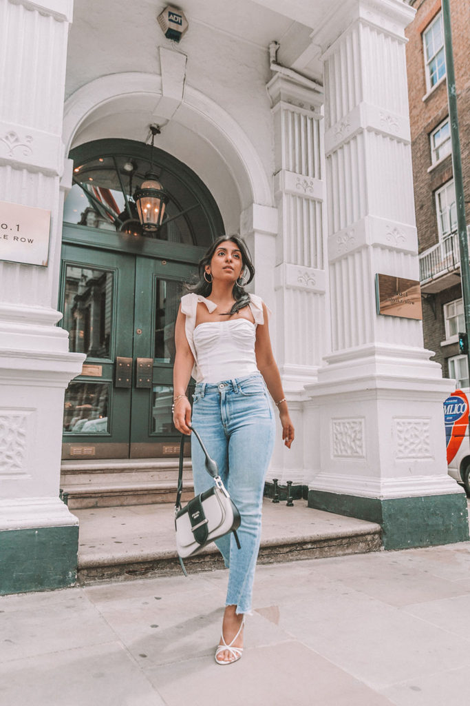 Luxury fashion blogger Shloka Narang of The Silk Sneaker shares a cute summer outfit for the heatwave styling blue jeans with a white summer blouse featuring Paige and Prada