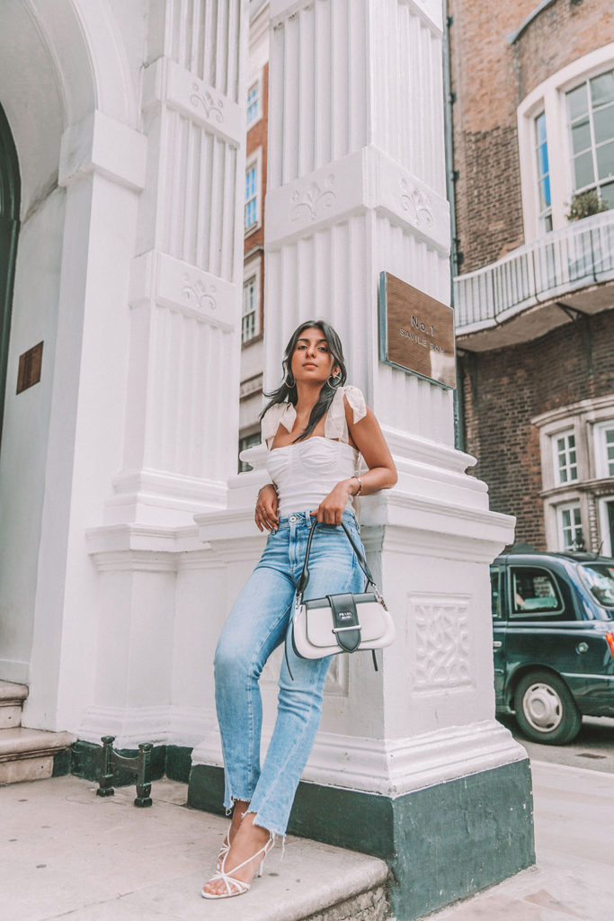 Luxury fashion blogger Shloka Narang of The Silk Sneaker shares a cute summer outfit for the heatwave styling blue jeans with a white summer blouse featuring Paige and Prada