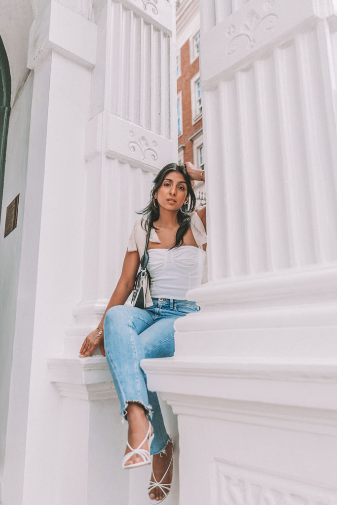 Luxury fashion blogger Shloka Narang of The Silk Sneaker shares a cute summer outfit for the heatwave styling blue jeans with a white summer blouse featuring Paige and Prada