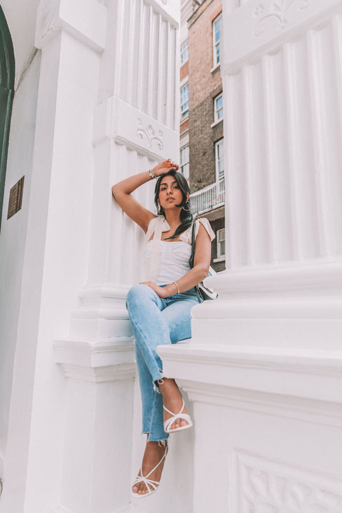 Luxury fashion blogger Shloka Narang of The Silk Sneaker shares a cute summer outfit for the heatwave styling blue jeans with a white summer blouse featuring Paige and Prada