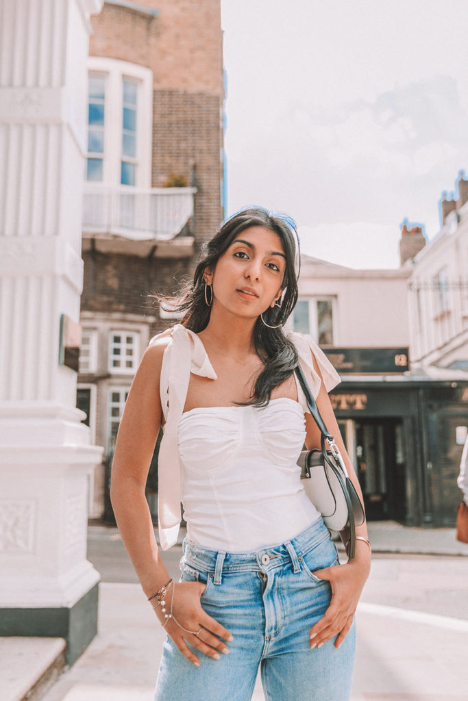 Luxury fashion blogger Shloka Narang of The Silk Sneaker shares a cute summer outfit for the heatwave styling blue jeans with a white summer blouse featuring Paige and Prada