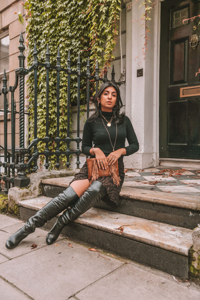 Luxury fashion blogger Shloka Narang of The Silk Sneaker shares a zebra print outfit in a ba&sh zebra print skirt with a turtleneck and thigh high boots