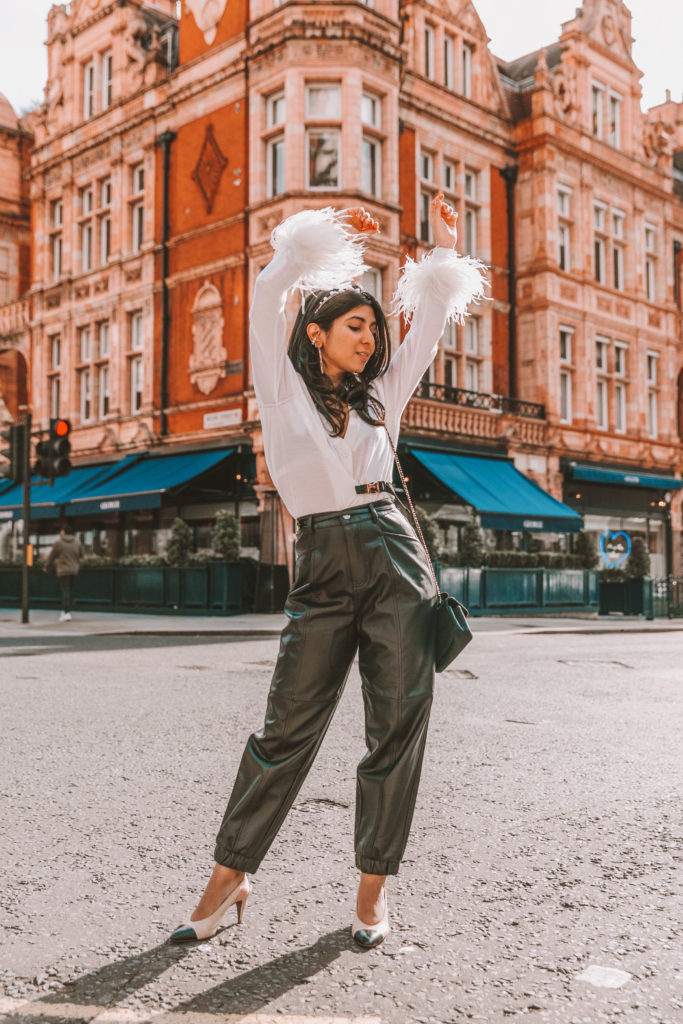 Luxury fashion blogger Shloka Narang of The Silk Sneaker shows how to style fall winter fashion trend of feathers wearing Prada sweater and Zara faux leather trousers