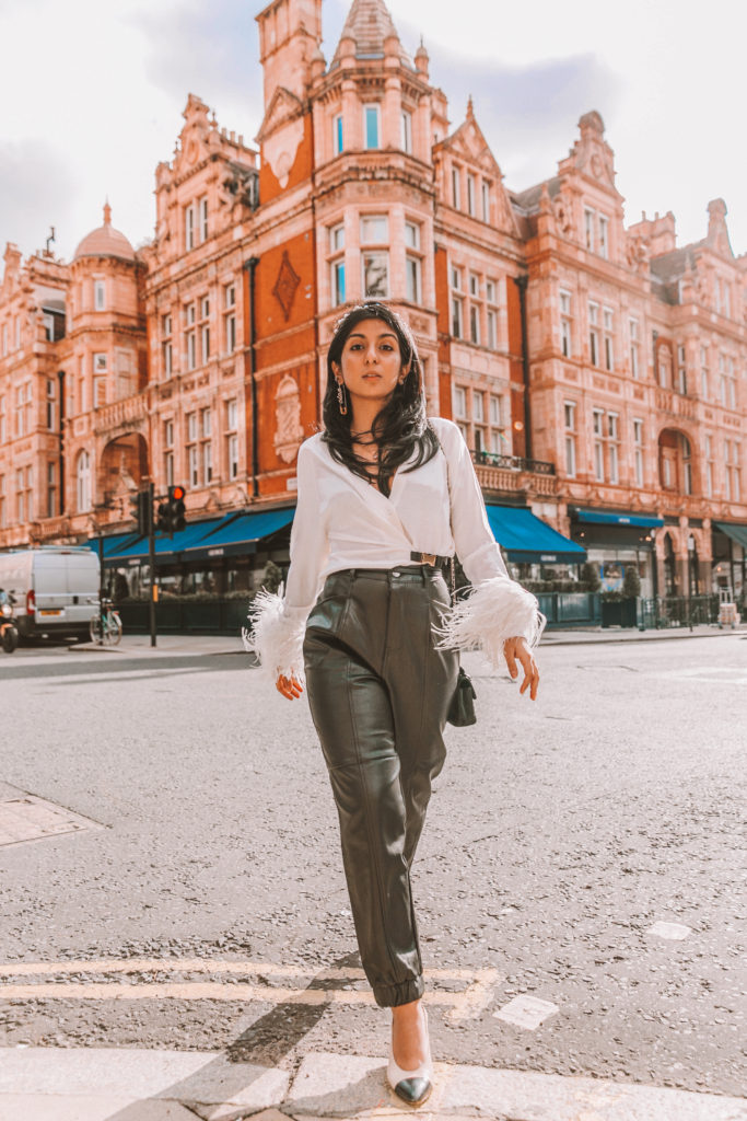 Luxury fashion blogger Shloka Narang of The Silk Sneaker shows how to style fall winter fashion trend of feathers wearing Prada sweater and Zara faux leather trousers