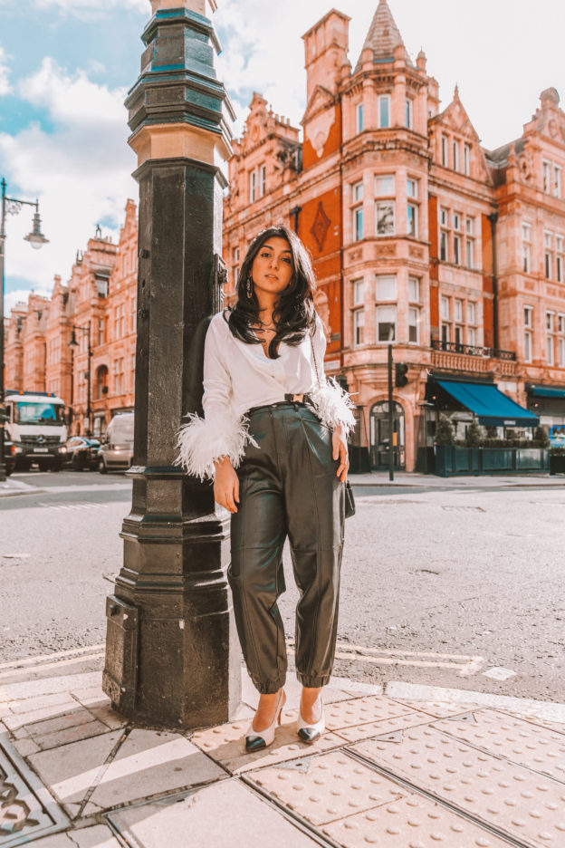 Luxury fashion blogger Shloka Narang of The Silk Sneaker shows how to style fall winter fashion trend of feathers wearing Prada sweater and Zara faux leather trousers
