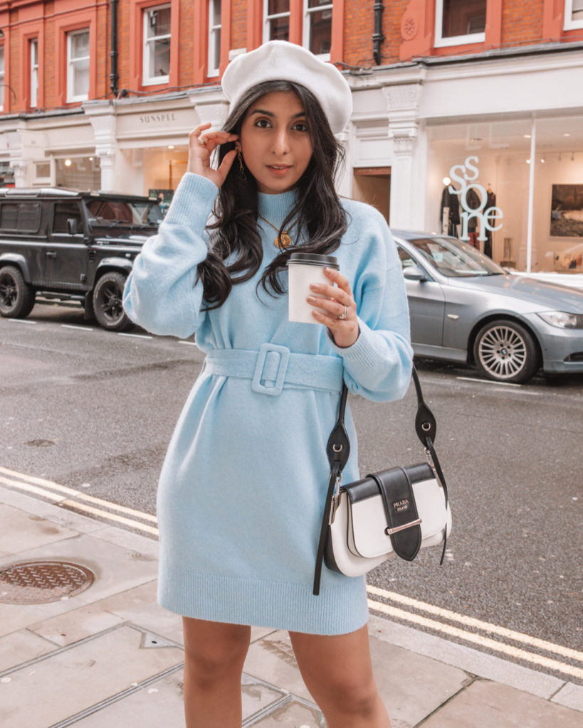 Luxury fashion blogger Shloka Sensarma of the Silk Sneaker styles an & Other Stories belted blue sweater dress with a Prada Sidonie Bag